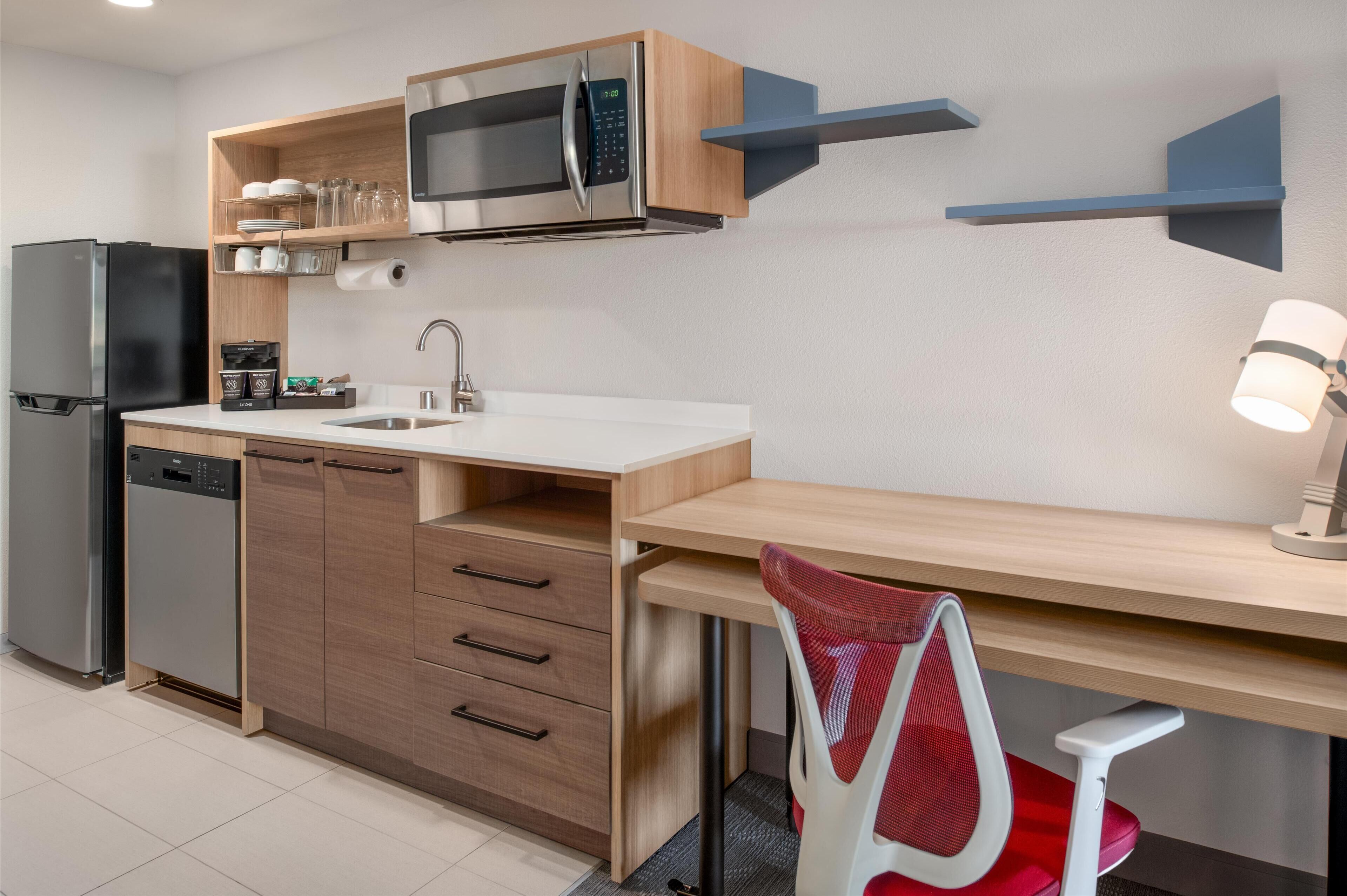 Cozinha moderna com micro-ondas embutido, frigorífico e máquina de lavar loiça. Existe bancada de madeira com uma pia e uma cadeira.