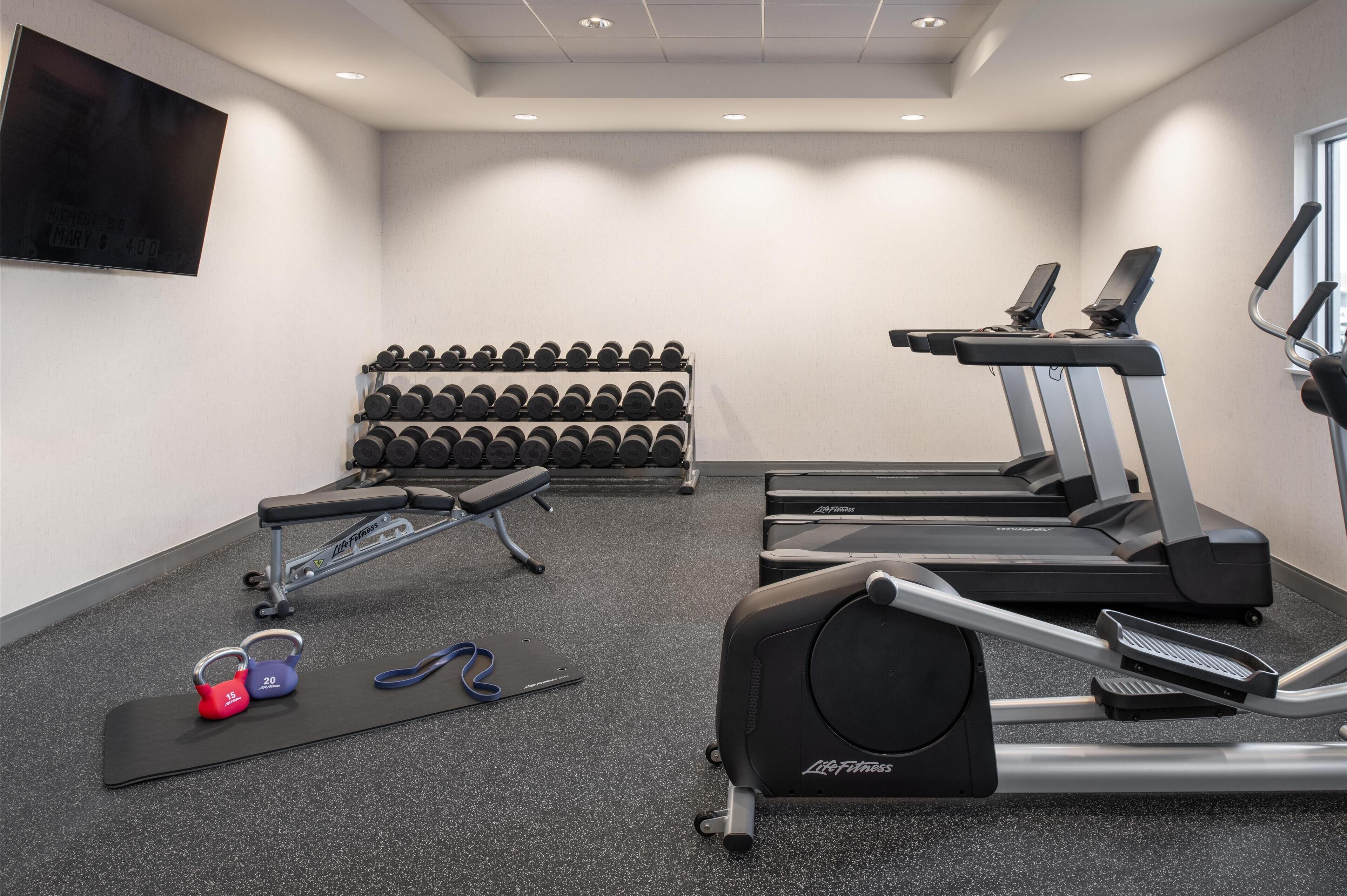A gym with treadmills, dumbbells, and a bench.