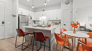 Een moderne keuken met witte kasten, een centraal eiland en oranje stoelen.