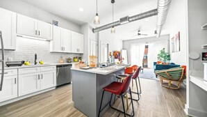Een moderne keuken met witte kasten, een centraal eiland met barstoelen en een eethoek met een blauwe bank en een rieten stoel.