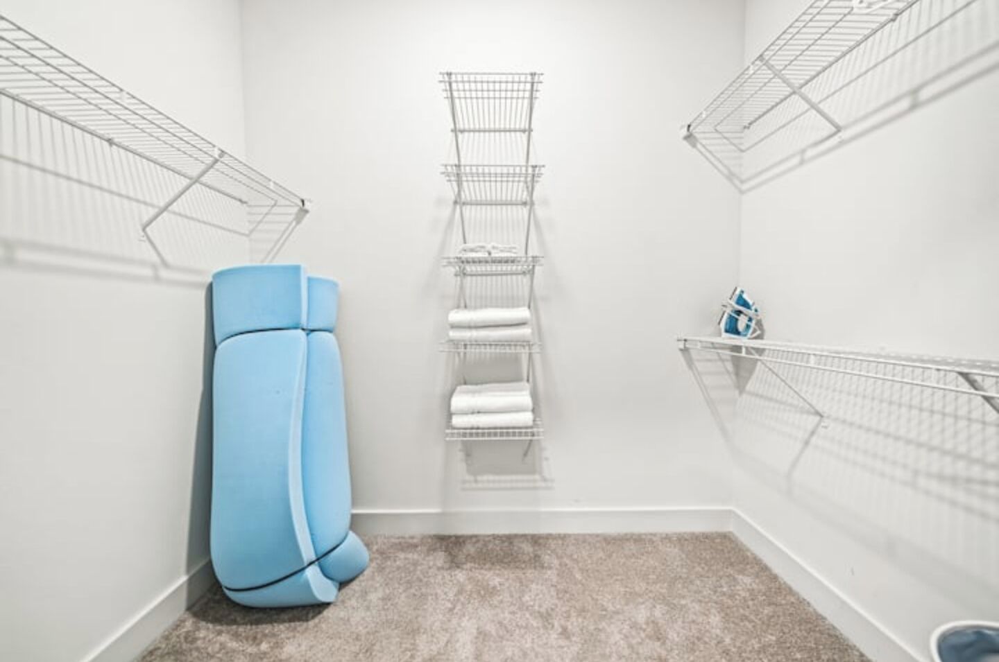 A small, well-lit room with a blue exercise ball, a metal rack with folded towels, and a metal shelf with a blue object.