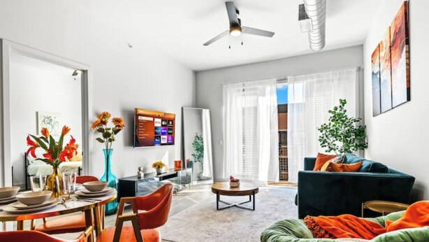 Een moderne woonkamer met een bank, fauteuils, een salontafel en een aan de muur bevestigde televisie.