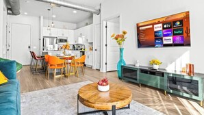 Een moderne woonkamer met een eethoek, een keuken op de achtergrond, en een televisie waarop diverse streamingdiensten worden getoond.