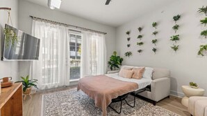 Un dormitorio moderno con cama, televisor, escritorio y una composición vegetal en la pared.
