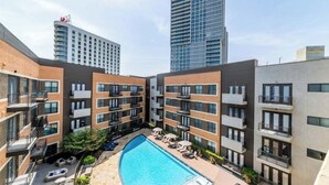 Un moderno edificio de apartamentos con piscina en un patio central, balcones y vistas de edificios altos circundantes.