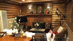 Ein gemütliches Blockhaus-Interieur mit einem Holzesstisch, Stühlen, einem Fernseher und einem Kamin mit dekorativen Steinen.