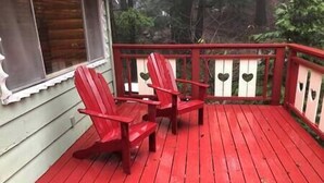 Eine rote Holzterrasse mit zwei Adirondack-Stühlen und einem weißen Geländer mit herzförmigen Ausschnitten.