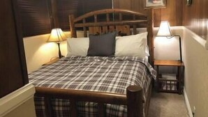 Ein hölzernes Himmelbett mit einem Karomuster-Bettüberwurf, zwei Nachttischlampen und einem kleinen Nachttisch mit einer Lampe.