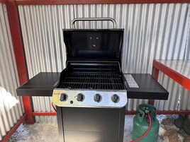 Una parrilla de gas Char-Broil con cuatro quemadores, una mesita lateral y un tanque de propano.