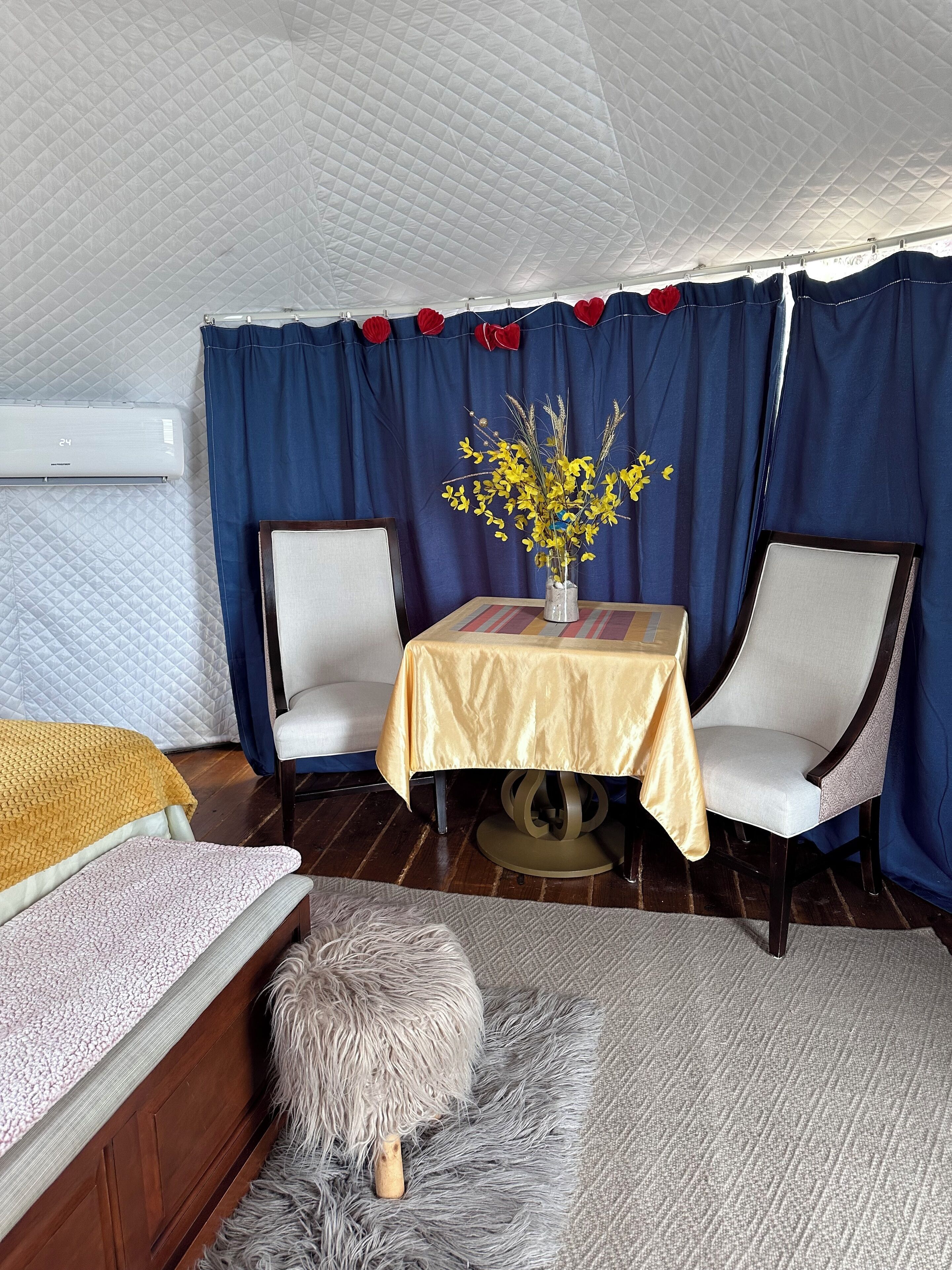 Una habitación acogedora con cama, dos sillas, una mesita con un florero y un ventilador de techo.