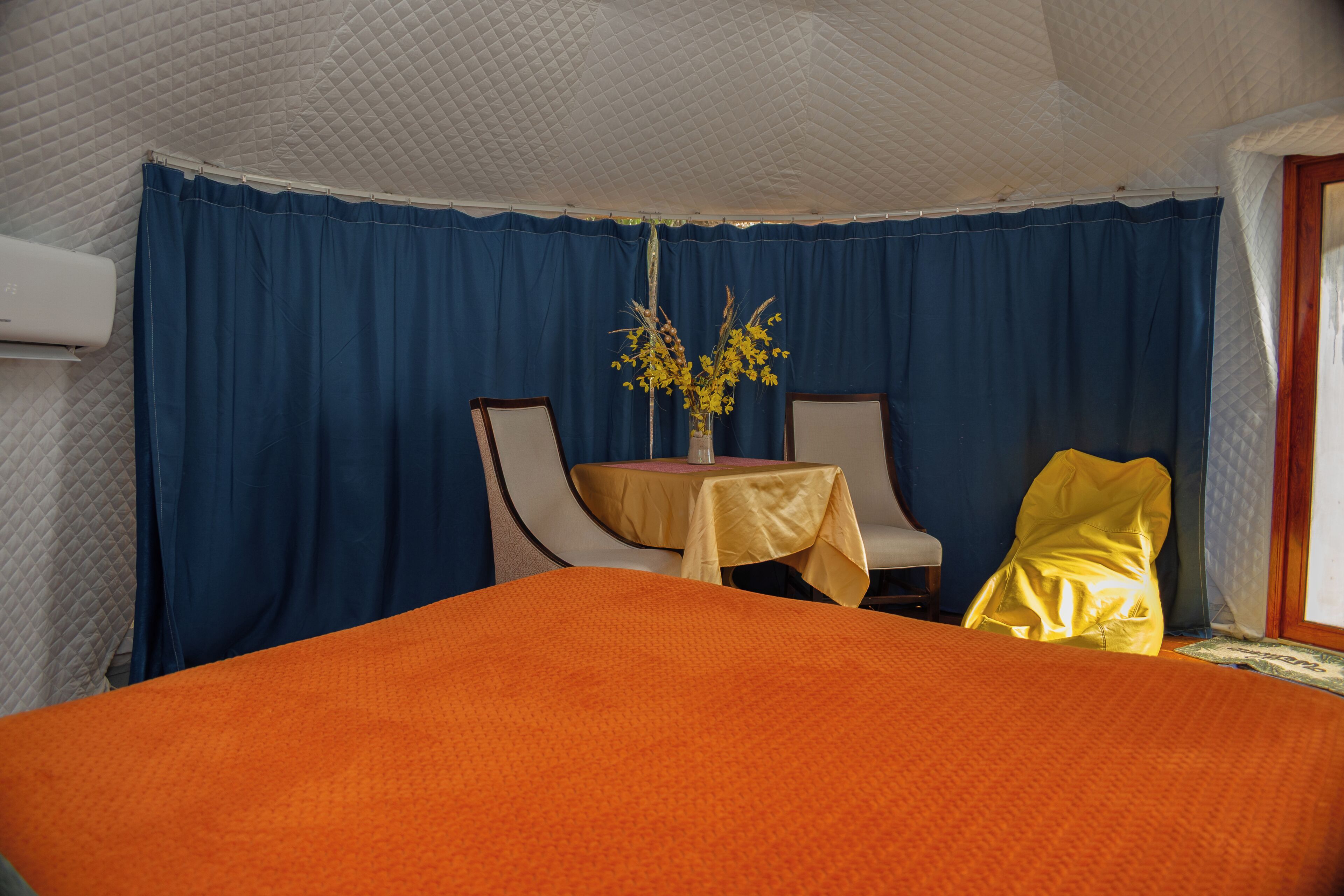 Quarto com cama, mesa com cadeiras e um vaso com flores.