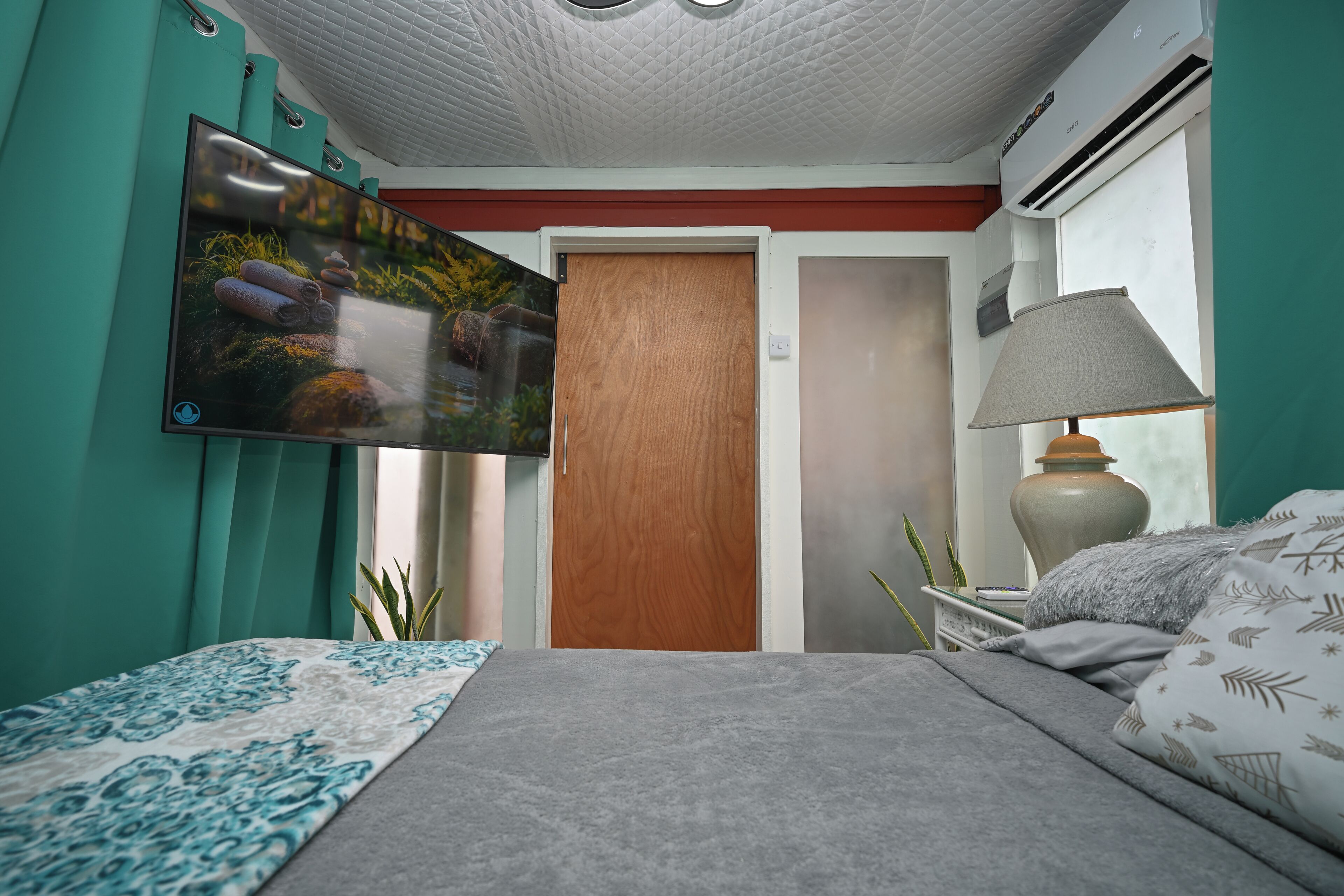 Quarto com cama, TV na parede, ar condicionado e abajur.