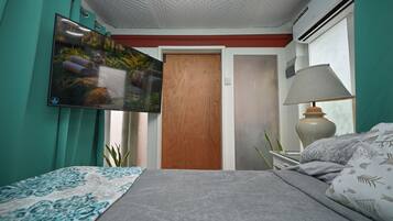 Quarto com cama, TV na parede, ar condicionado e abajur.