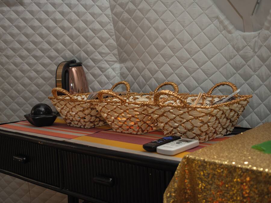 A bed with a quilted headboard, a bedside table with a remote control, a black lamp, and a decorative basket.