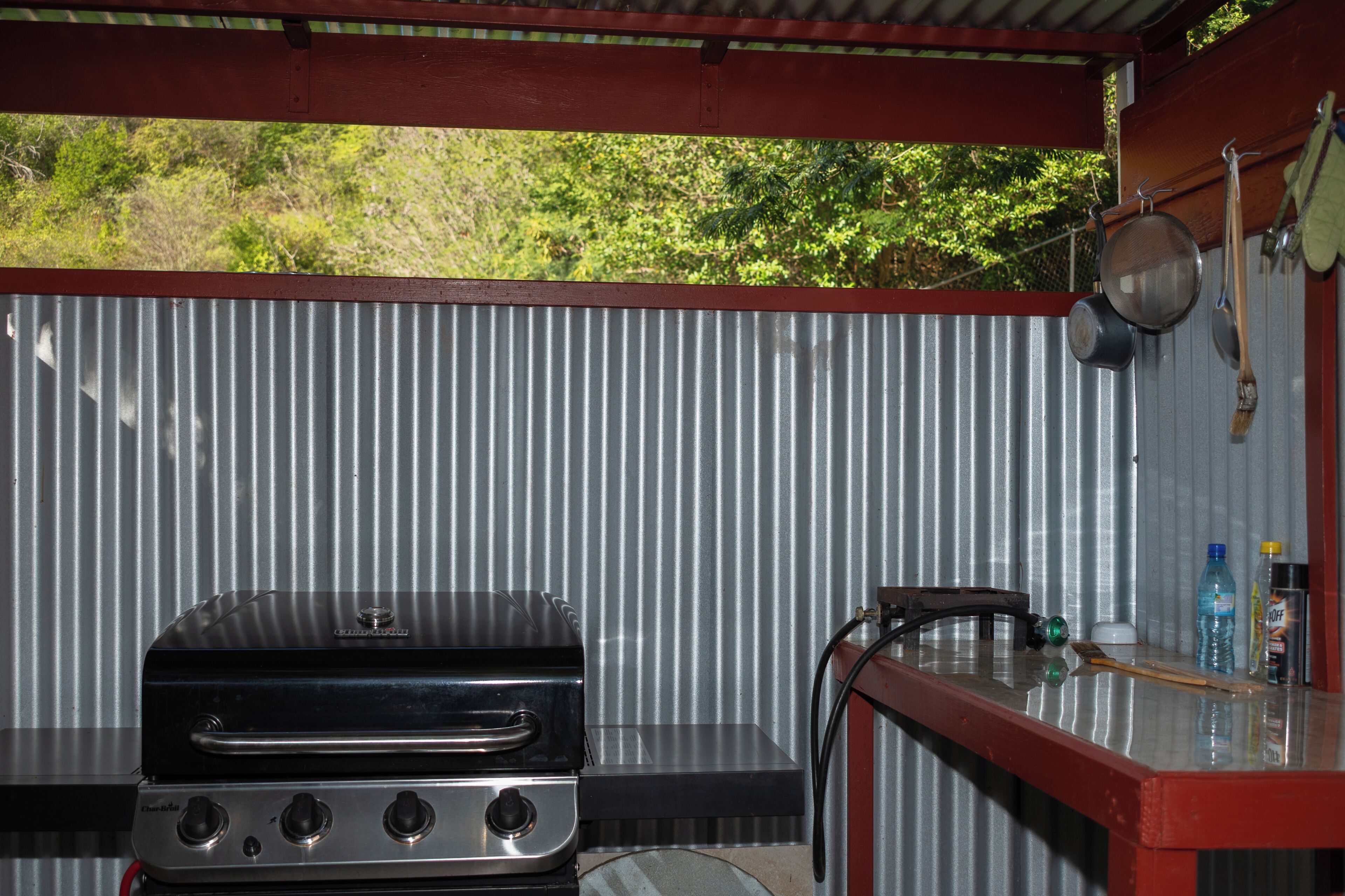 Una barbacoa, una paret metàl·lica i una taula petita amb estris de cuina.