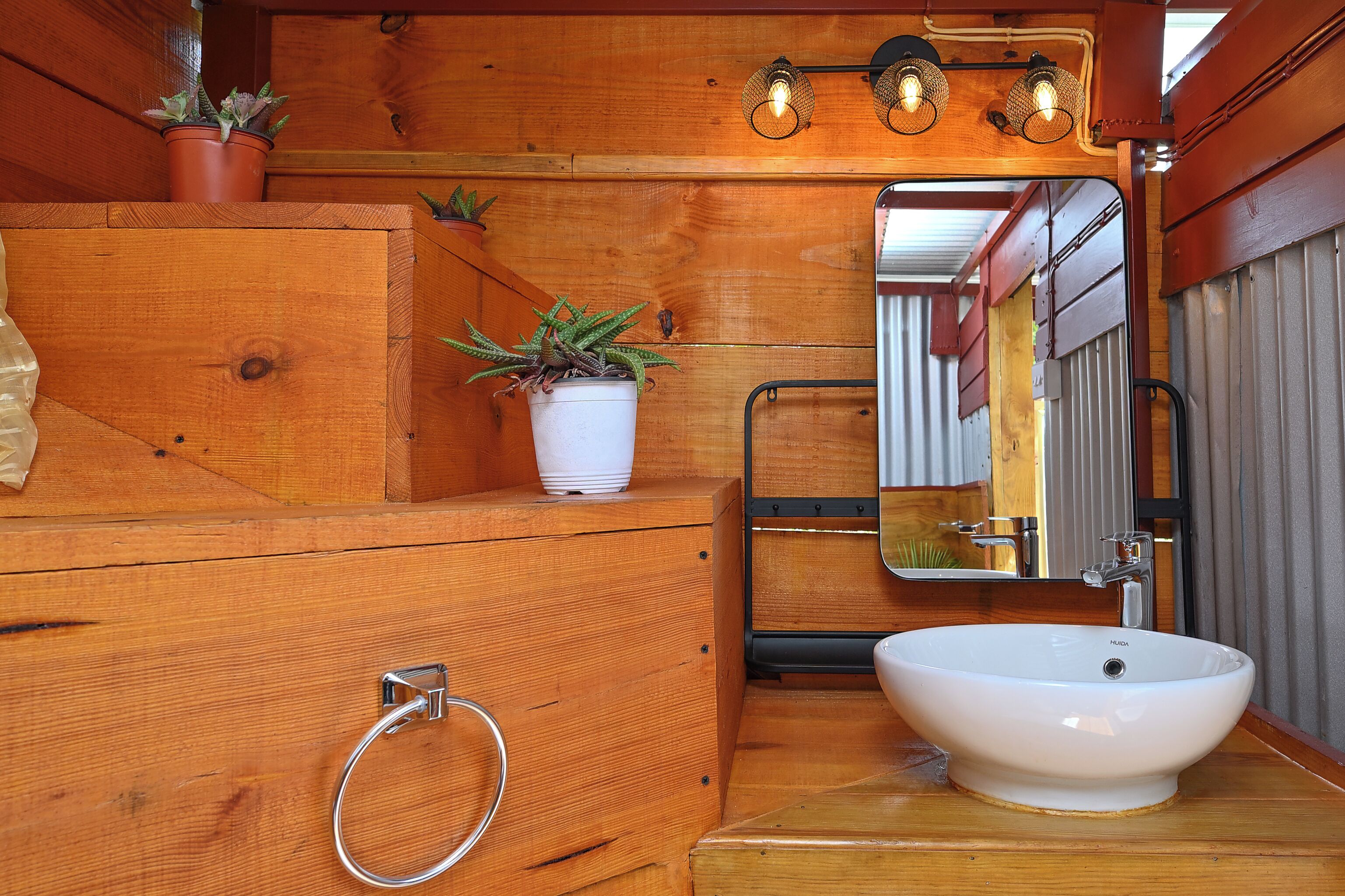 A wooden bathroom with a white sink, a mirror, and two potted plants.