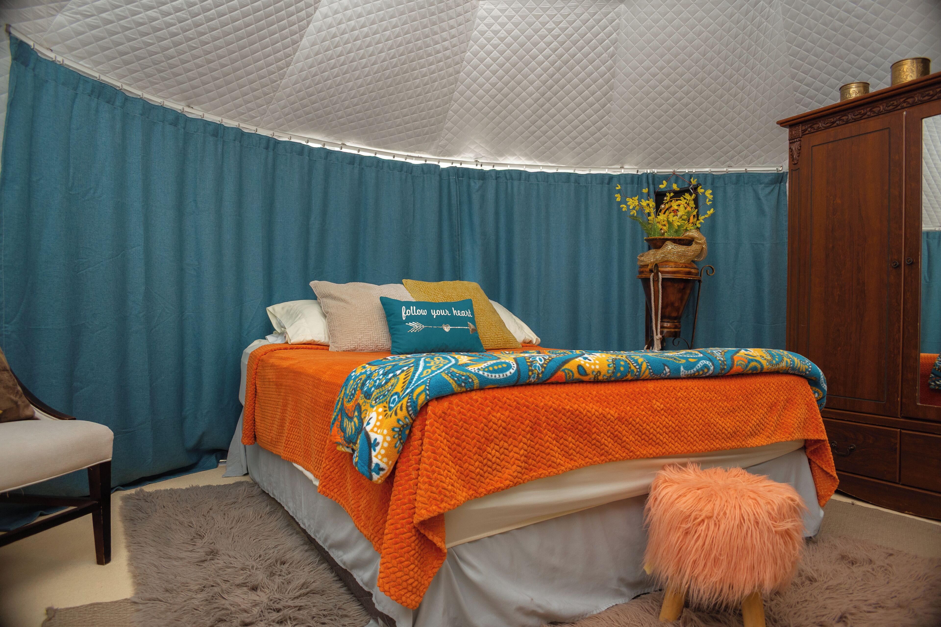 A bedroom with a bed, a chair, a wardrobe, and a decorative vase.