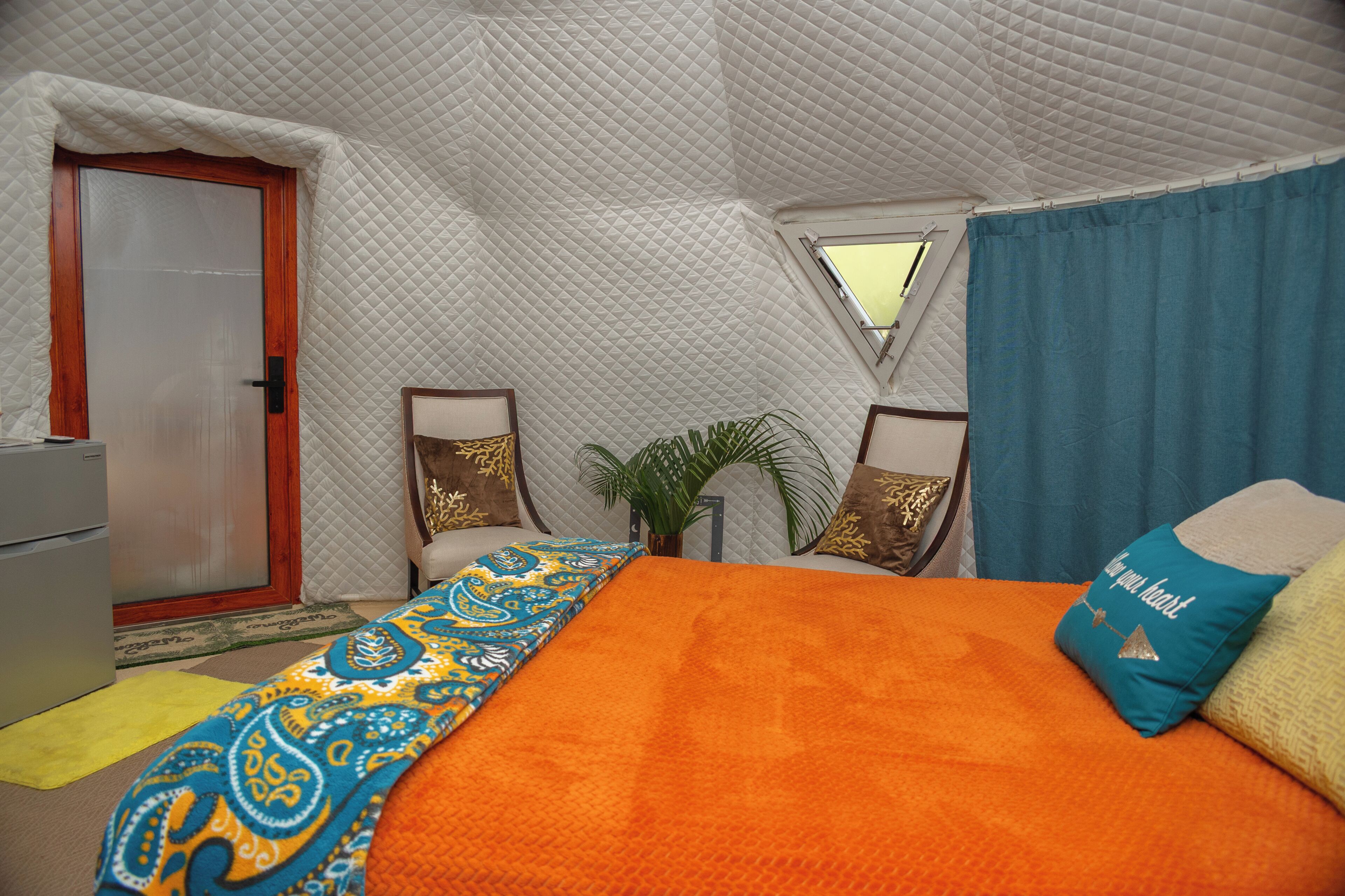 Una habitación tipo tienda de campaña con cama, puerta, ventana y una pequeña mesa.
