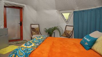 Una habitación tipo tienda de campaña con cama, puerta, ventana y una pequeña mesa.