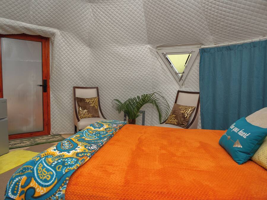 Una habitación tipo tienda de campaña con cama, puerta, ventana y una pequeña mesa.