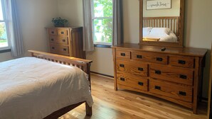 Une chambre à coucher avec un lit, une commode en bois et un miroir orné d’une inscription.