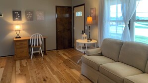 Un salon chaleureux avec un plancher en bois, un canapé beige, un bureau avec une chaise et une lampe.