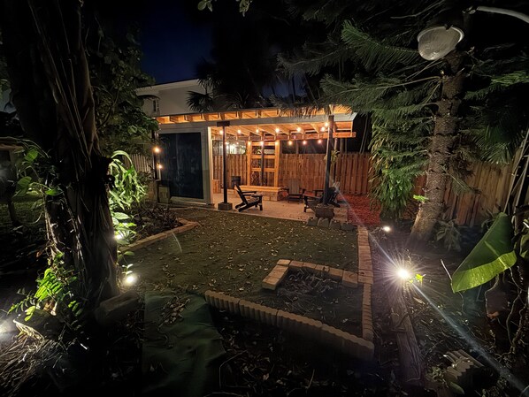 Un patio exterior moderno con terraza de madera, zona de estar e iluminación ambiental.