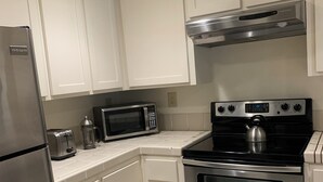 A kitchen with white cabinets, a stainless steel refrigerator, a microwave, a stove, and an oven. - Adorable condo with WiFi in charming neighborhood (Richmond)