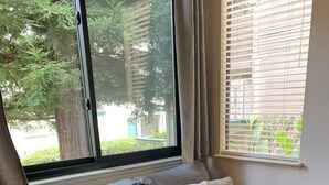 A grey sofa with patterned cushions, a window with blinds, and a view of greenery outside. - Adorable condo with WiFi in charming neighborhood (Richmond)