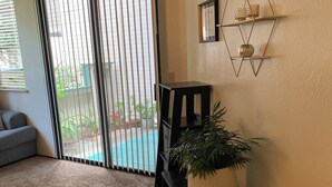 A living room with a large sliding glass door leading to a balcony, a black side table with a potted plant, and a geometric wall decoration. - Adorable condo with WiFi in charming neighborhood (Richmond)