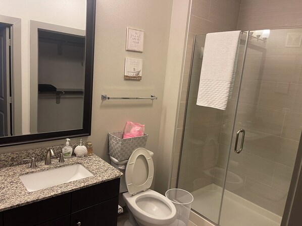 A bathroom with a granite countertop sink, a toilet, a glass shower enclosure, and a towel hanging on the shower door. - Cozy 2B2B Pool/Skyline View Near Galleria Mall (Houston)