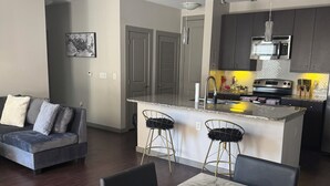 Une cuisine moderne avec un îlot central, un parquet en bois foncé, une table à manger en marbre et un canapé gris dans l’espace salon.