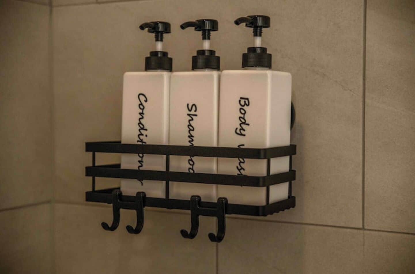 A bathroom shelf holding three bottles of shampoo and conditioner.