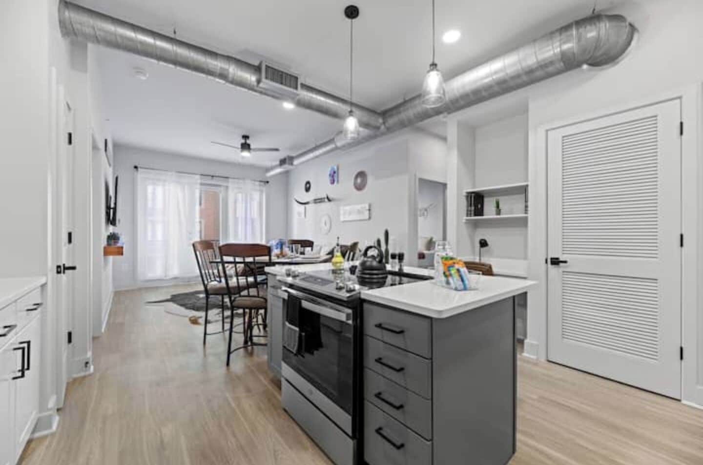 A modern kitchen with a central island, a dining area with chairs, and a hallway leading to a door.