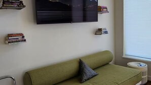 Een moderne woonkamer met een groene bank, een wandgemonteerde televisie en boekenkasten.