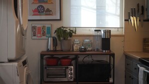 Una cucina compatta con forno tostatutto, macchina del caffè e una pianta in vaso su un tavolino.