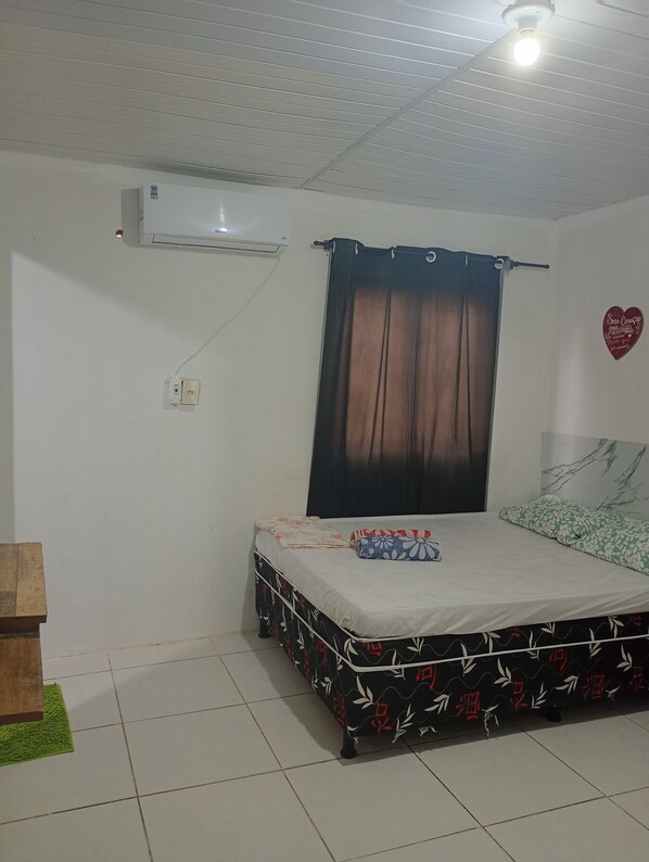 A bedroom with a bed, a ceiling fan, an air conditioner, a curtain, a heart-shaped decoration, and a green rug. - Pousada sol e luar (Recife)