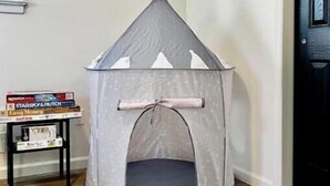 A corner room with a grey tent-like playhouse, a small table with books, and a door.