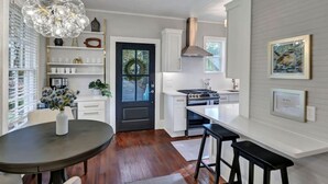 A modern kitchen with white cabinetry, a black door, and a dining area with a round table and bar stools. - The Wren + Nest | Main & Guest House | Sleeps 10 (Columbia)