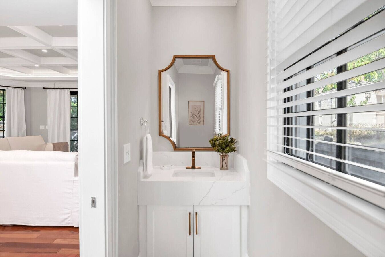 Une salle de bain moderne avec un meuble-lavabo blanc, un miroir à cadre doré et une plante en pot.