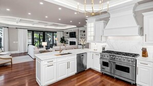 A spacious kitchen with white cabinetry, a central island, stainless steel appliances, and a chandelier. - The Wren + Nest | Main & Guest House | Sleeps 10 (Columbia)