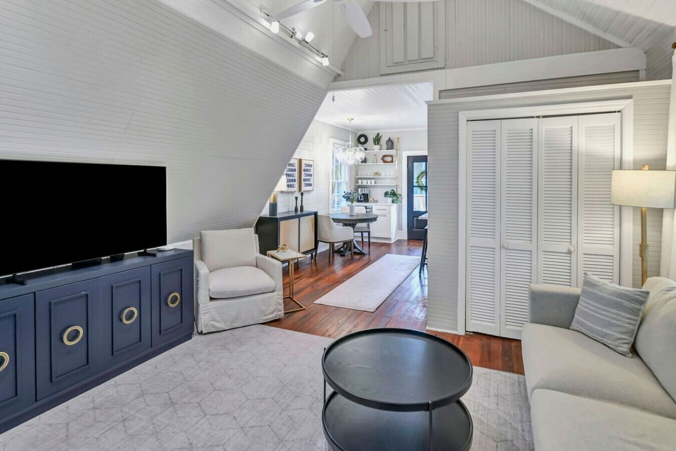 A spacious living room with a large flat-screen TV, a dark blue cabinet with gold handles, a round black coffee table, and a light-colored sofa.