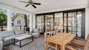 A covered patio with a wooden table and chairs, a sofa, and wicker chairs. - The Wren + Nest | Main & Guest House | Sleeps 10 (Columbia)