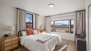 A bedroom with a large bed, two bedside tables, a nightstand, a window with a view of mountains, and a gray sofa. - Family-Friendly 4BR Provo Home Close to Provo Airport (Provo)