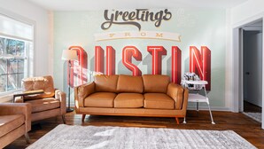 Un salon avec un canapé en cuir marron, une petite chaise blanche, un lampadaire et un mur orné d’une affiche sur laquelle on peut lire : « Salutations d’Austin ».