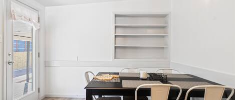 A dining area with a black table, white chairs, and a white door with a view of the outside.