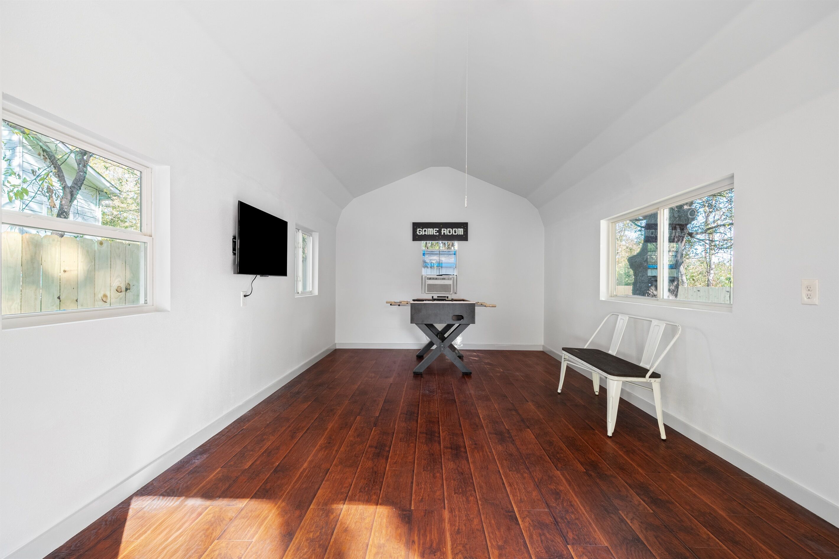 Una stanza con pavimento in legno, una panca, un televisore e un cartello con scritto 'GAME ROOM'.