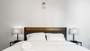 Un lit bien fait, avec du linge de lit blanc, deux lampes de chevet et une tête de lit en bois.
