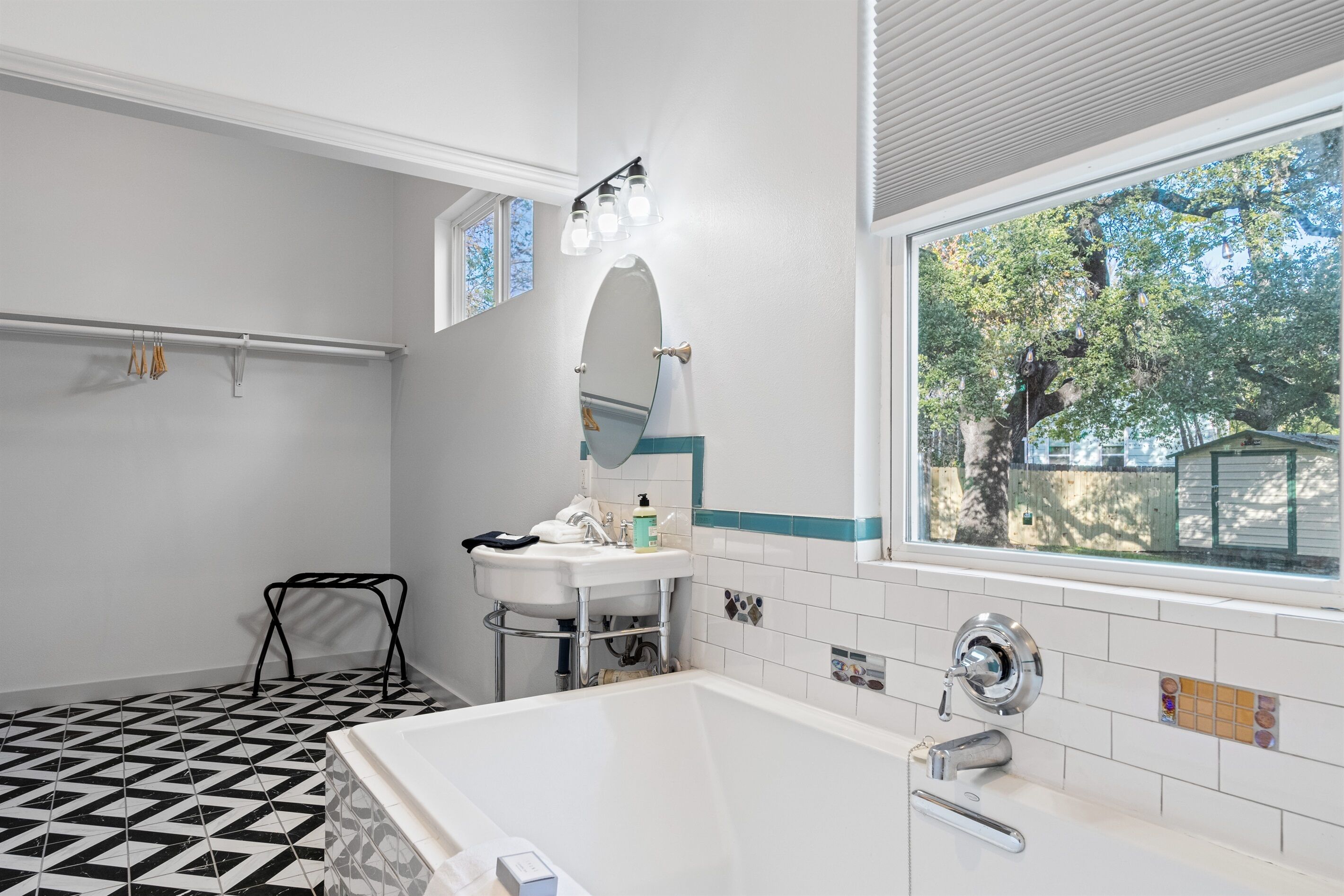 Ein Badezimmer mit Waschbecken, Spiegel, Badewanne und Fenster mit Blick auf Bäume.