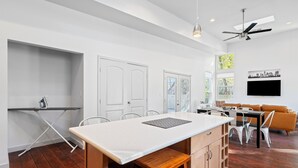 A modern kitchen with a large island, white cabinetry, and a dining area with a sofa and chairs. - Austin Gated Oasis | 4BR | Sleeps 8 | Fire Pit (Austin)
